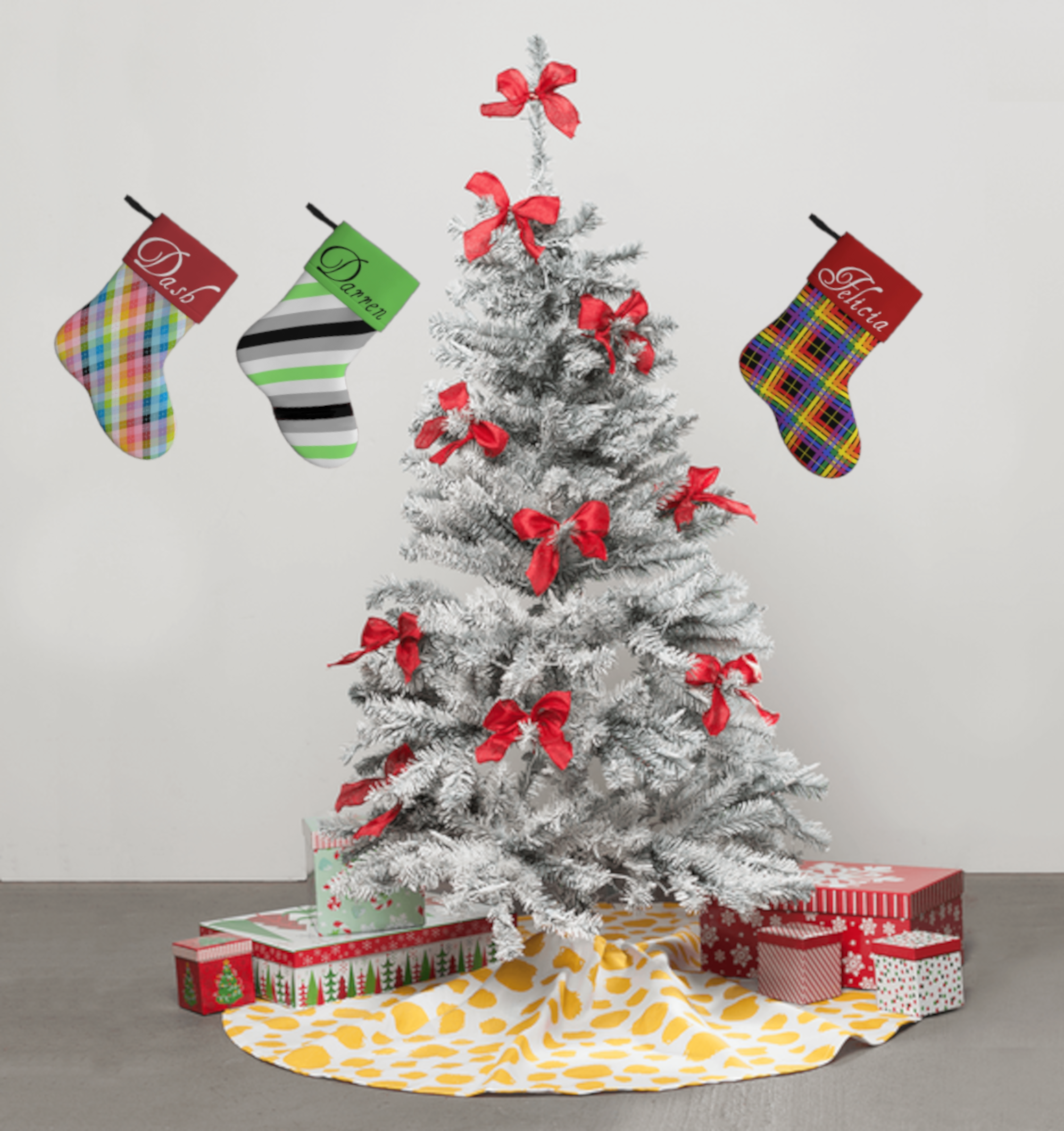 Image of a white Christmas tree with red bows on the branches. There are red and white presents sitting below the tree, on a yellow polka-dotted tree skirt. On the wall behind the tree, three stockings are hanging.