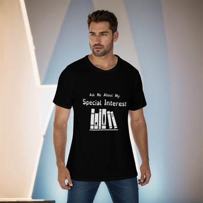 Mockup of a masc-presenting model with short dark hair and evening shadow, wearing a black tshirt with white logo and text. Text: Ask Me About My Special Interest. Logo, below: 6 Stylized books on a shelf.