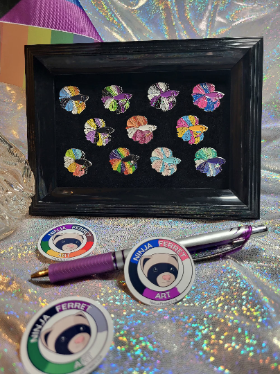 Pride-themed enamel betta fish pins with glitter fins, shown on a black background in a black picture frame.