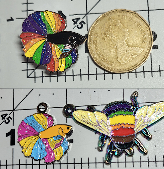 Split phto showing a rainbow betta pin next to a Canadian loonie ($1 coin). The lower photo shows a pansexual betta pendant beside a rainbow bumblebee pendant. Both bettas are approximately 1" wide.
