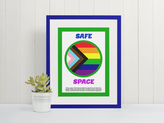 Image of a Safe Space poster in a blue fram, sitton on a white table with a small plant beside it.
