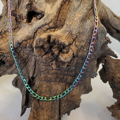 A rainbow-plated steel figaro chain necklace draped over a piece of driftwood.